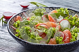 Tasty salad with natural ingredients - lettuce, slices of radish, peices of grapefuits, cheese in the ceramic bowl on a