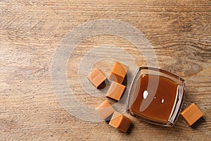 Tasty salted caramel in glass bowl and candies on wooden table, flat lay. Space for text