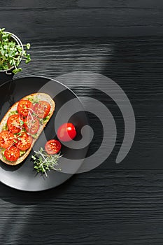 Tasty sandwich with cherry tomatoes, micro greens and avocado on wholegrain bread on black wooden background. Healthy delicious