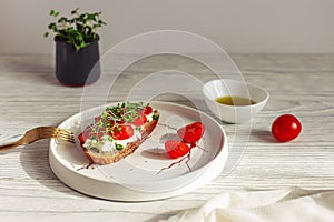 Tasty sandwich with cherry tomatoes, micro greens and soft cheese on wholegrain bread on light wooden background. Healthy