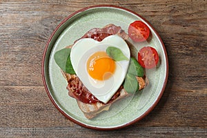 Tasty sandwich with heart shaped fried egg and  bacon on wooden table, top view