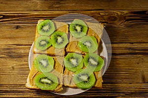 Tasty sandwiches with peanut butter and kiwi fruits on wooden table. Top view