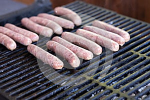Tasty sausages sizzling on a portable BBQ fire grilling over the flames on a summer picnic, close up view.preparing bbq