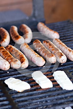 Tasty sausages sizzling on a portable BBQ fire grilling over the flames on a summer picnic, close up view.preparing bbq