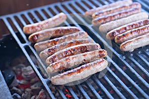 Tasty sausages sizzling on a portable BBQ fire grilling over the flames on a summer picnic, close up view.preparing bbq