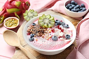 Tasty smoothie bowl with fresh kiwi fruit, berries and granola on pink wooden table, closeup