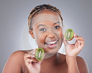Tasty source of fibre. Studio shot of an attractive young woman holding kiwi fruit to her face against a grey background