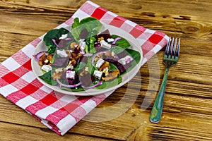 Tasty spinach salad with boiled beetroot, feta cheese, walnut and red onion on wooden table. Healthy vegetarian food