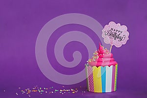 Tasty strawberry cupcake with sprinkles and Happy Birthday banner on violet background. Party background