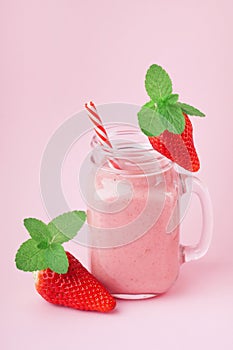 Tasty strawberry smoothie or milkshake in mason jar decorated mint on pink table. Healthy food for breakfast and snack.