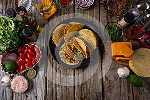 Tasty street tacos with beef, tomatoes, onion and cheese on black round plate. Ingredients for cooking tacos on rustic wooden