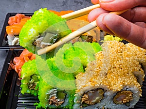 Tasty sushi bar, Eating Sushi with chopsticks. California Sushi roll set with salmon, vegetables, fish, caviar closeup. Japan