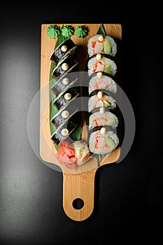 Tasty sushi roll futomaki with avocado and crab meat on wooden serving board on black background.