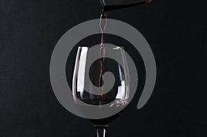 Tasty sweet red wine pouring into tha wineglass against black background