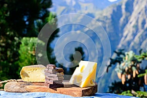 Tasty Swiss cheeses and dark pure chocolate, emmental, gruyere, appenzeller served outdoor with Alpine mountains peaks on
