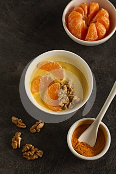 Tasty tangerine smoothie bowl with fruits, cereals, seeds and turmeric powder over grey background