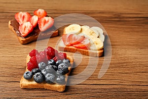 Tasty toasts with different spreads and fruits on wooden table. Space for text