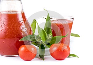 Tasty tomato juice in jug under water drops, glass juice, greens, two raw tomatoes isolated white background