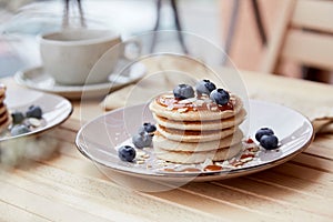 Tasty traditionalvegan pancakes with fresh blueberries and agave syrup on a plate. Cup of coffee on background