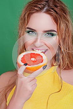 Tasty tropical fruits! Attractive sexual woman with beautiful makeup and wet hair eating fresh juicy grapefruit or orange smiling