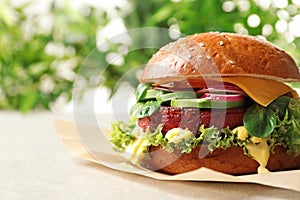 Tasty vegetarian burger with beet cutlet on table against blurred background.