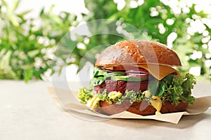 Tasty vegetarian burger with beet cutlet on table against blurred background.