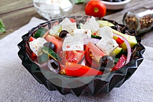 Tasty  vitamin salad with fresh vegetables, goat cheese, black olives, basil sauce on a white plate on a wooden background