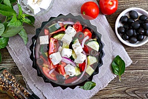 Tasty  vitamin salad with fresh vegetables, goat cheese, black olives, basil sauce on a white plate on a wooden background. Top