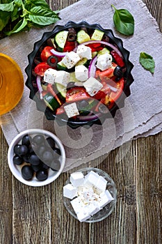 Tasty  vitamin salad with fresh vegetables, goat cheese, black olives, basil sauce on a white plate on a wooden background. Top