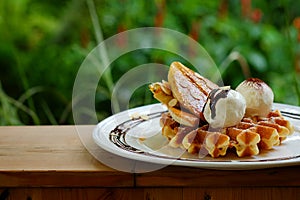 Tasty waffle and vanilla ice cream set served with banana sugar coating Topped with chocolate sauce on white plate in green garden