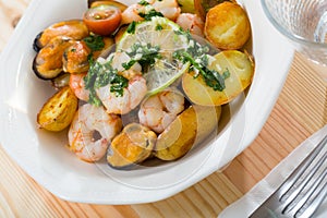 Tasty warm salad with fried potatoes, shrimp and mussels, served at plate