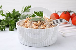 Tasty wheat porridge with parsley in bowl on white table, closeup
