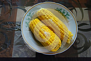 Tasty yellow boiled Ukrainian two pumpkins of corn and salt laid out on plates with green flowers.