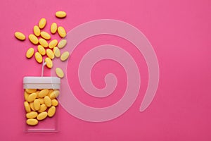 Tasty yellow dragee candies and container on pink background, flat lay. Space for text