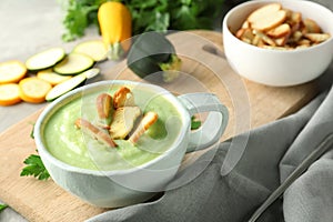Tasty zucchini soup with croutons in cup on wooden board