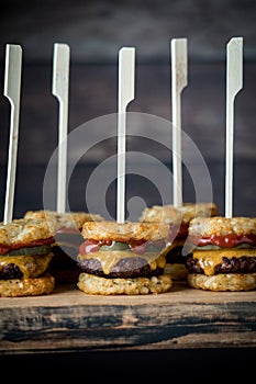 Tater and beef slider skewers on a wooden board, against a dark background.