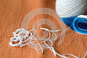 Tatting lace in the manufacturing process. Fragment of lace and shuttle on textile background close-up. Hobbies and leisure