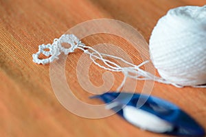 Tatting lace in the manufacturing process. Fragment of lace and shuttle on textile background close-up. Hobbies and leisure