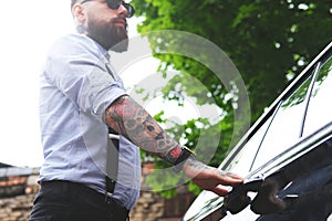Tattoed bearded man is opening his car.