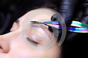 Tattoo artist holds a small pair of scissors in his hand and cuts off the tip of the eyebrow hairs photo