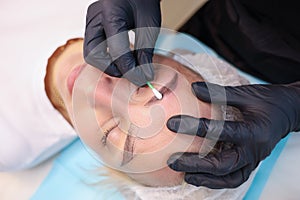 Tattoo artist wipes the newly made permanent makeup of the eyebrows with a cotton swab