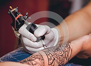 Tattoo master protective gloves make a tattoo in black ink on the hand of the girl.