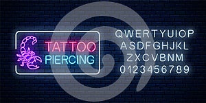 Tattoo and piercing parlor glowing neon signboard with scorpio emblem and alphabet. Tattooing salon sign