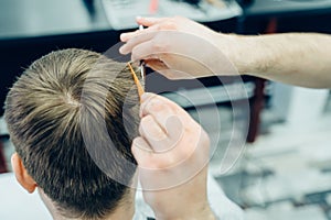 Tattooed Barber cuts the hair of the client with scissors. Close up. Attractive male is getting a modern haircut in