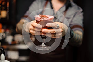 Tattooed barman hands holding a cocktail glass