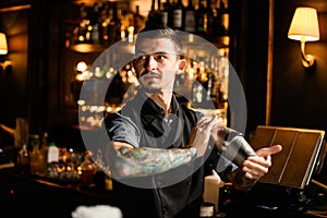 Tattooed bartender holding in hands a steel shaker with a deliciouds cocktail