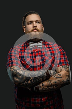 Tattooed bearded unformal male in red shirt and grey bow tie.