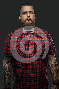 Tattooed bearded unformal male in red shirt and grey bow tie.