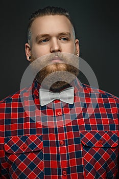 Tattooed bearded unformal male in red shirt and grey bow tie.