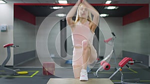 Tattooed blond beautiful slim Caucasian young woman stepping on gym cube training indoors. Portrait of fit confident